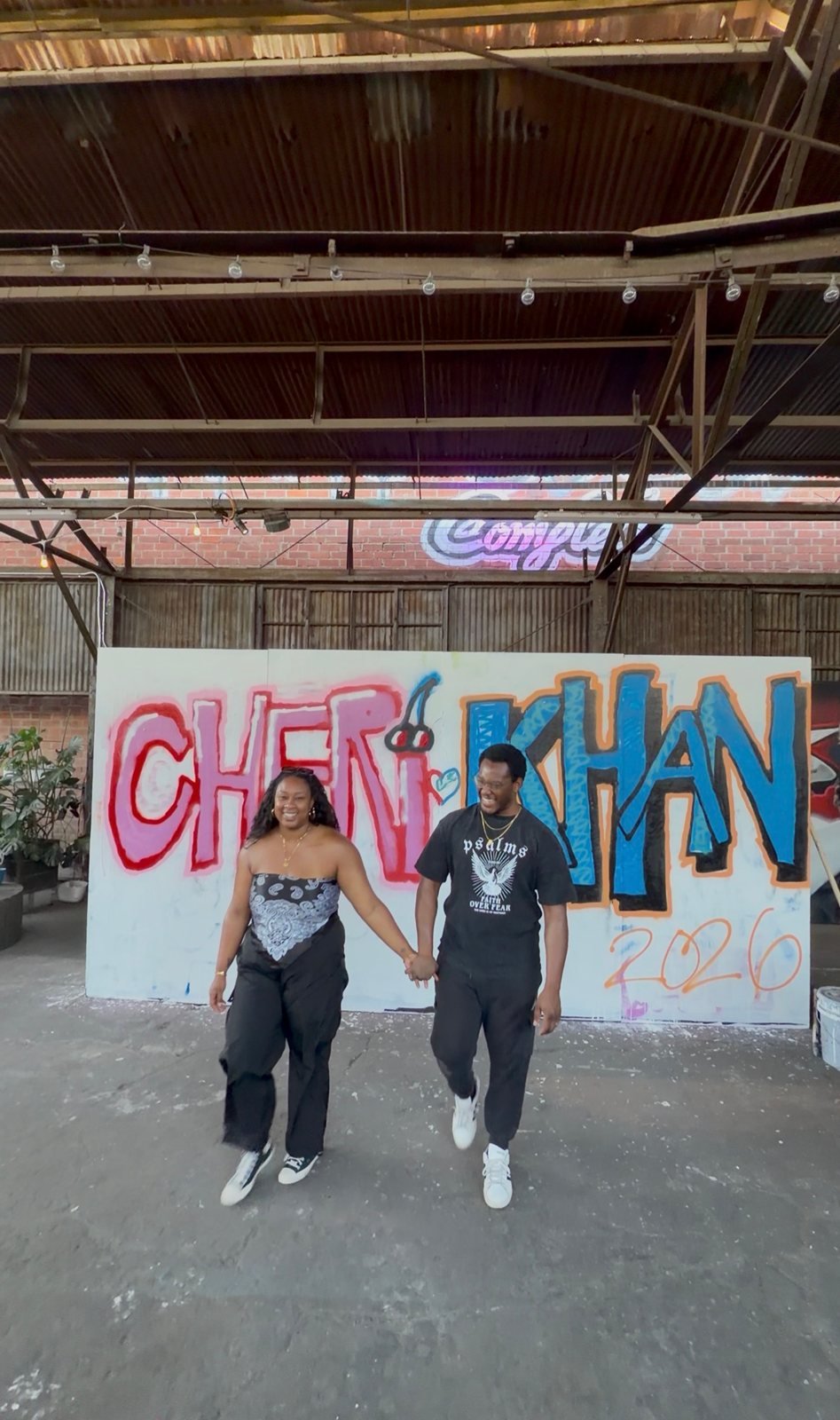 Two workshop guests holding hands in front of their pink and blue graffiti pieces