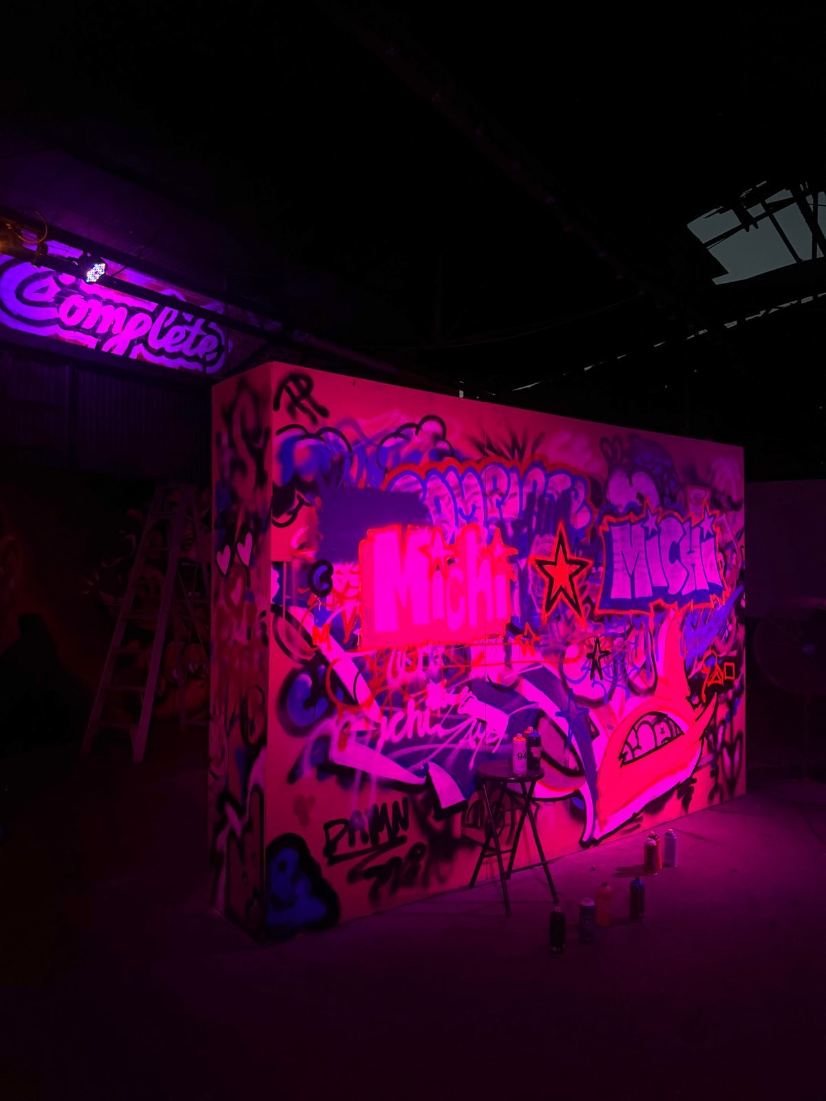 Freestanding graffiti wall and spray cans under pink lighting at Complete Studio