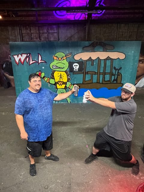 Two workshop guests celebrating beside their illustrated graffiti wall