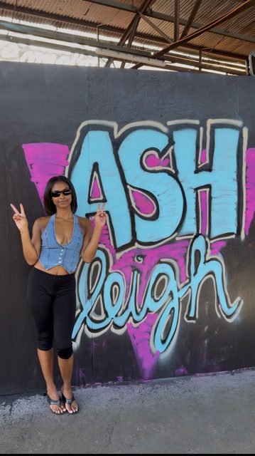 Workshop guest beside a blue and pink ASH graffiti piece