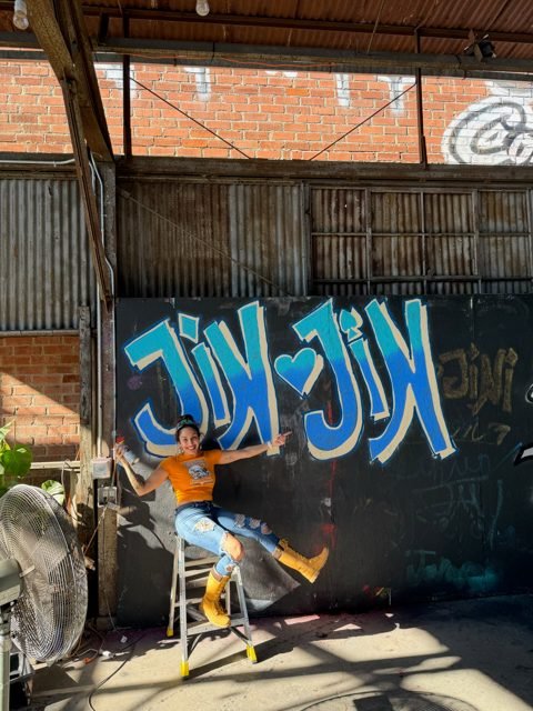 Workshop guest posing beside blue graffiti lettering