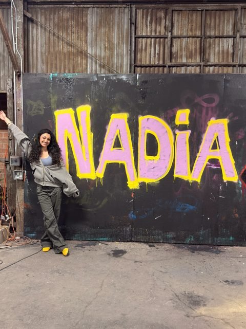 Workshop guest beside a yellow and pink NADIA graffiti piece
