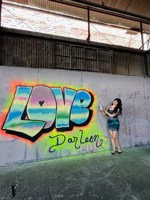 Workshop guest beside a rainbow LOVE graffiti piece
