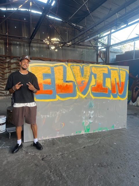 Workshop guest beside an orange and yellow MELVIN graffiti piece